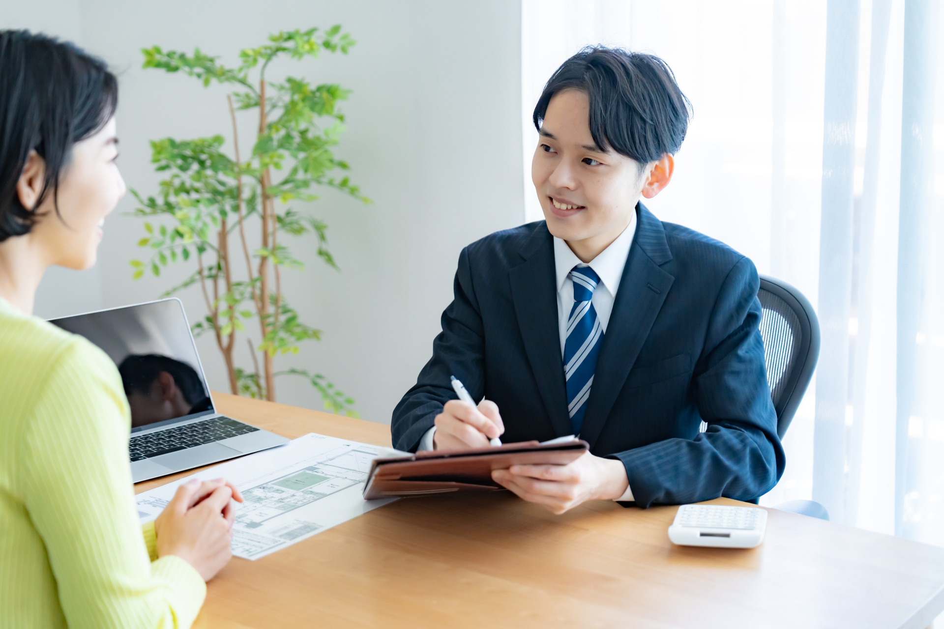 書類を挟んで打ち合わせをする不動産担当者と相談者